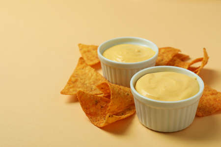 Bowls with cheese sauce and chips on beige background