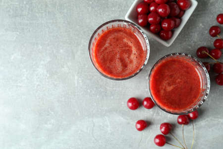Glasses of cherry smoothie and ingredients on gray textured tableの写真素材