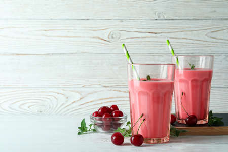 Glasses of cherry smoothie and ingredients on white wooden tableの写真素材