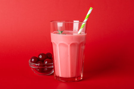 Glass of cherry smoothie and ingredients on red backgroundの写真素材