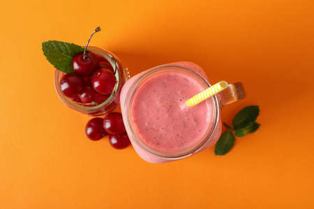 Glass jar of cherry smoothie and ingredients on orange backgroundの写真素材
