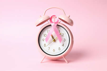Breast cancer awareness ribbon and alarm clock on pink background