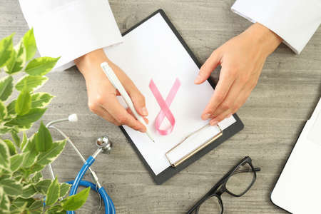 Female doctor hands and breast cancer awareness ribbon on workplace backgroundの写真素材