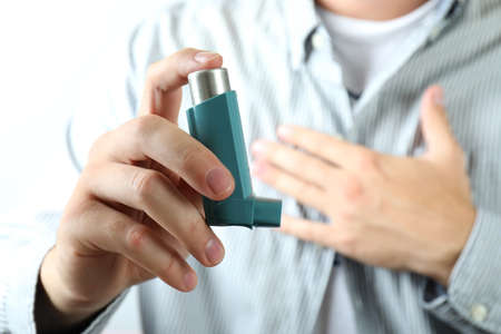 Young man holds asthma inhaler during asthma attackの写真素材