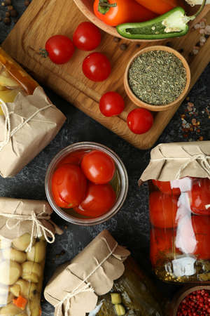 Jars of pickled vegetables and ingredients on black smokey table