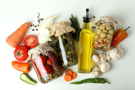 Jars of pickled vegetables and ingredients on white table