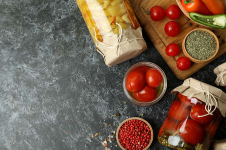 Jars of pickled vegetables and ingredients on black smokey table