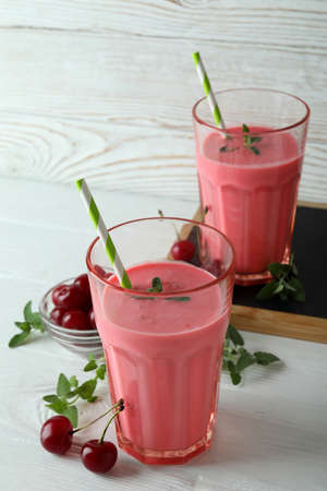 Glasses of cherry smoothie and ingredients on white wooden tableの写真素材
