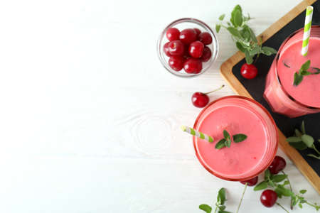 Glasses of cherry smoothie and ingredients on white wooden tableの写真素材