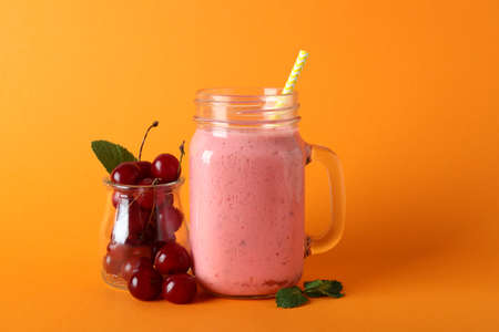 Glass jar of cherry smoothie and ingredients on orange backgroundの写真素材