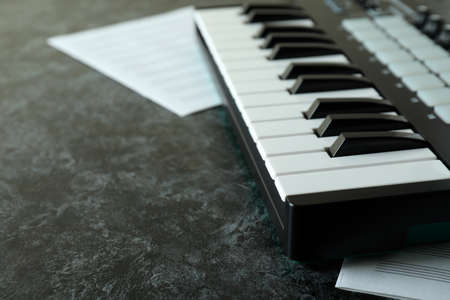 Midi keyboard and music sheets on black smokey tableの写真素材