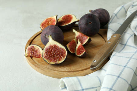 Board with fig, knife and kitchen towel on white textured table
