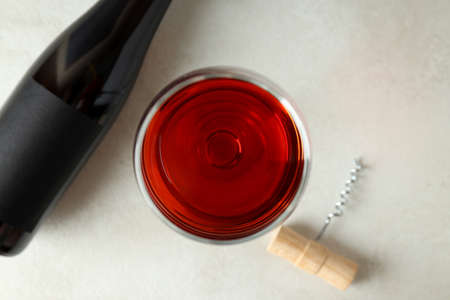 Bottle and glass of wine, and corkscrew on white textured table