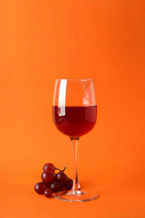 Glasses of red wine and grape on orange backgroundの写真素材