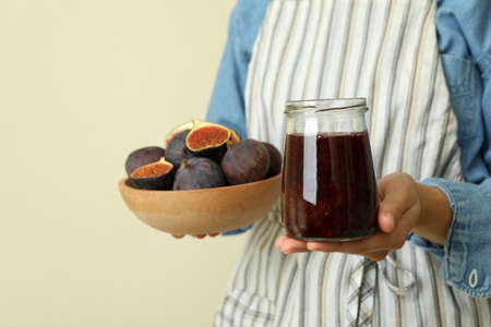 Woman in apron holds jar of fig jam and bowl with figの写真素材