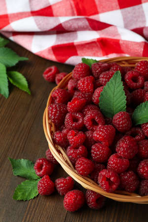 Raspberries in a wicker bowl and a tea towel on a wooden table.