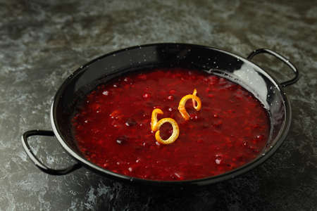 Dish with cranberry sauce and orange peel on black smokey background