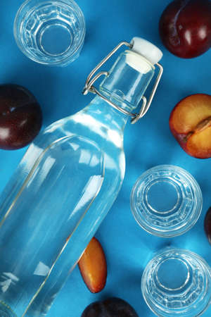 Bottle and shots of plum vodka and ingredients on blue backgroundの写真素材