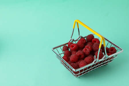 Red juicy raspberries in a shopping basket on a menthol background.の写真素材