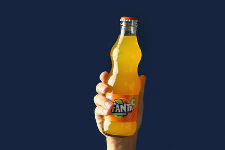 Odessa, Ukraine - September 23, 2021: Female hand holds Fanta bottle on blue background.のeditorial素材