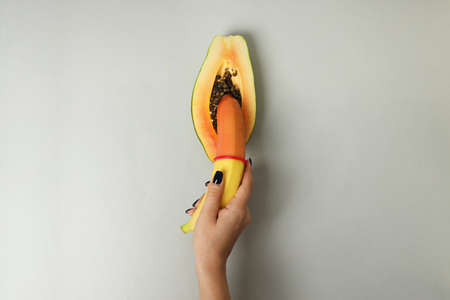 Female hand holding banana with condom in papaya on light gray backgroundの写真素材