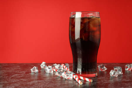Glass of cola, ice and straws against red background.