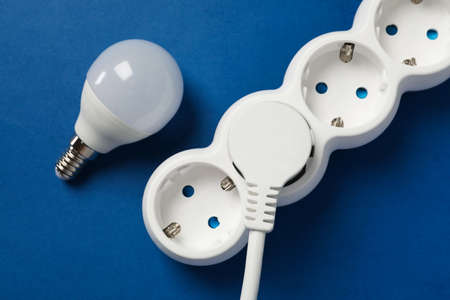 Energy saving bulb and power strip on blue background.