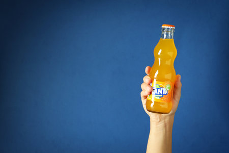 Odessa, Ukraine - September 23, 2021: Female hand holds Fanta bottle on blue background.