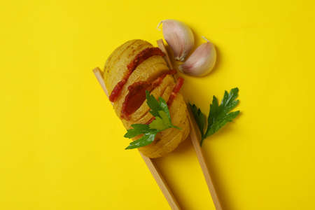 Wooden tongs with baked potato on yellow background.の写真素材
