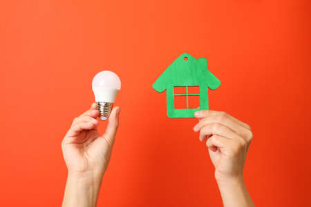 Hands hold energy saving bulb and house on red background.の写真素材