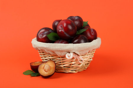 Wicker bowl with plums on an orange background.の写真素材