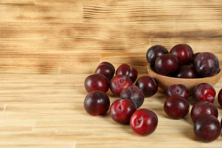 Plums in a wooden bowl on a wooden table.の写真素材
