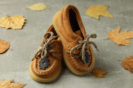 Baby shoes and leaves on gray textured background.