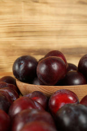 Plums in a wooden bowl on a wooden table.の写真素材