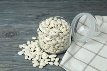 Jar with white beans on gray wooden background.