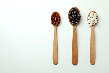 Spoons with different types of beans on white background
