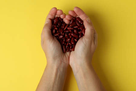 Female hands hold red beans on yellow background.の写真素材