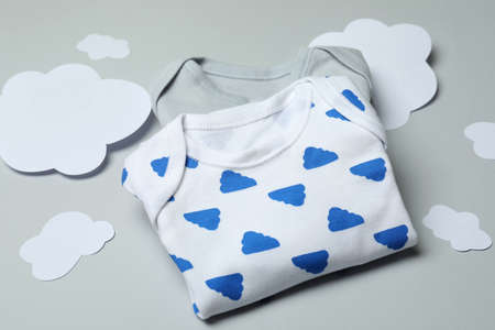 Baby clothes and decorative clouds on light gray background.