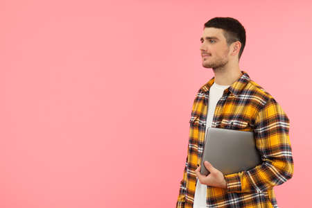 Young man with laptop on pink background, space for text.