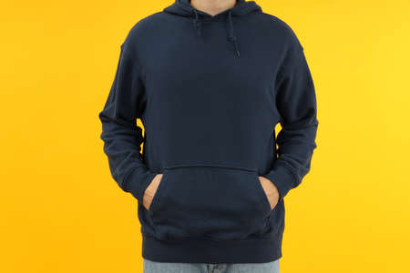 Man in hoodie with hands in pocket on yellow background.