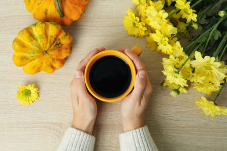 Female hands hold cup of coffee on wooden background with pumpkins and chrysanthemums.の写真素材