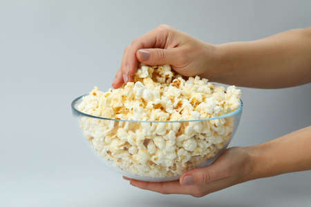 Female hands hold bowl with popcorn on light gray background.の写真素材