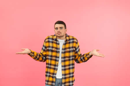 Young man in misunderstanding on pink background.の写真素材