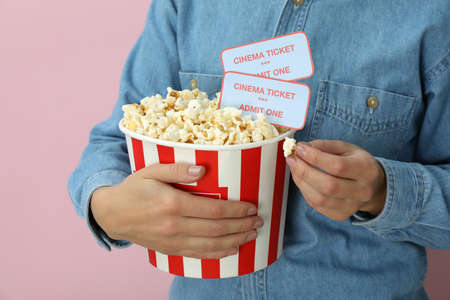 Woman holds paper cup with popcorn and tickets on pink background.の写真素材