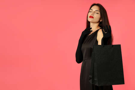 Attractive girl in black dress with paper bags on pink background.
