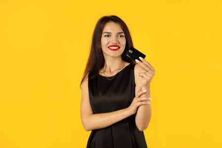 Girl in black dress with credit card on yellow background.の写真素材