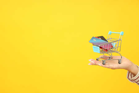 Female hand holds shop trolley with credit cards on yellow background.の写真素材