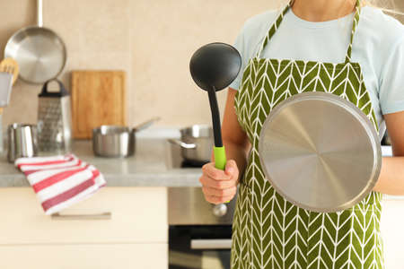 Woman in apron holds kitchen ladle and pot cap.の写真素材