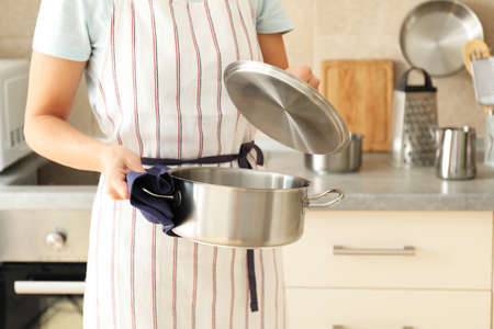 Woman in apron holds metal pot, space for text.