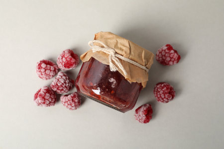 Jar of raspberry jam with ingredients on light gray background